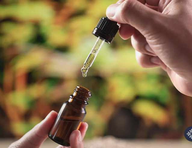 Amber glass dropper bottle with CBD oil tincture being dispensed, natural green background