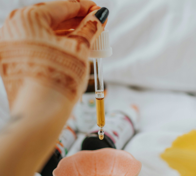 Person dispensing CBD oil drops from glass dropper against white background