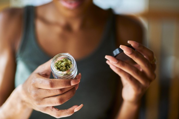 A woman opening a small container of Marijuana flower.