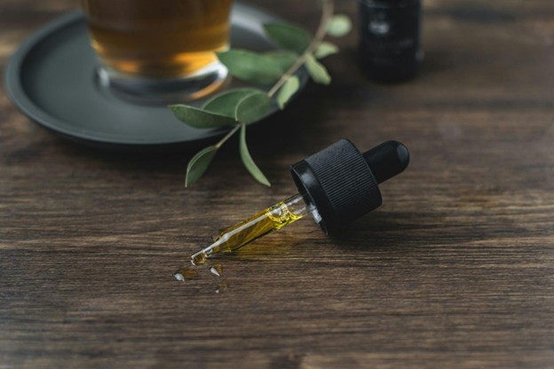 A glass vial full of CBD oil next to a plant.