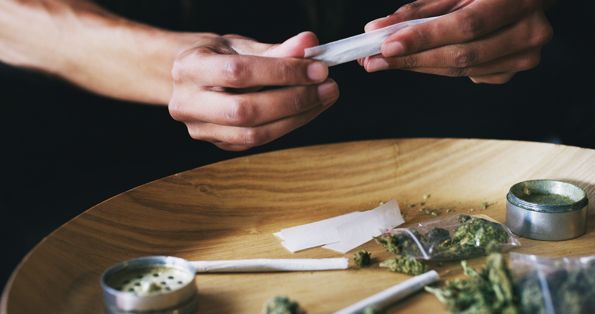 Hands wearings rings gently rolling a joint of ground THCA marijuana flower.
