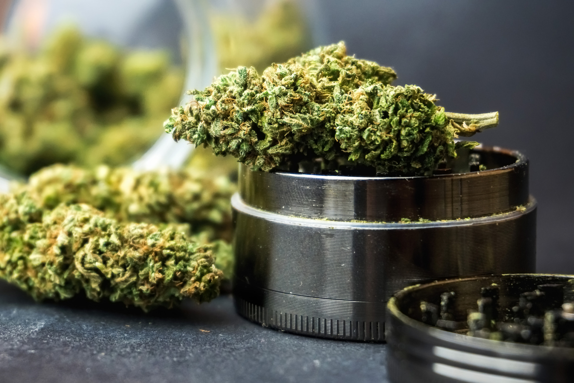 Medical THTCA marijuana flower buds in glass jar and grinder on dark backdrop