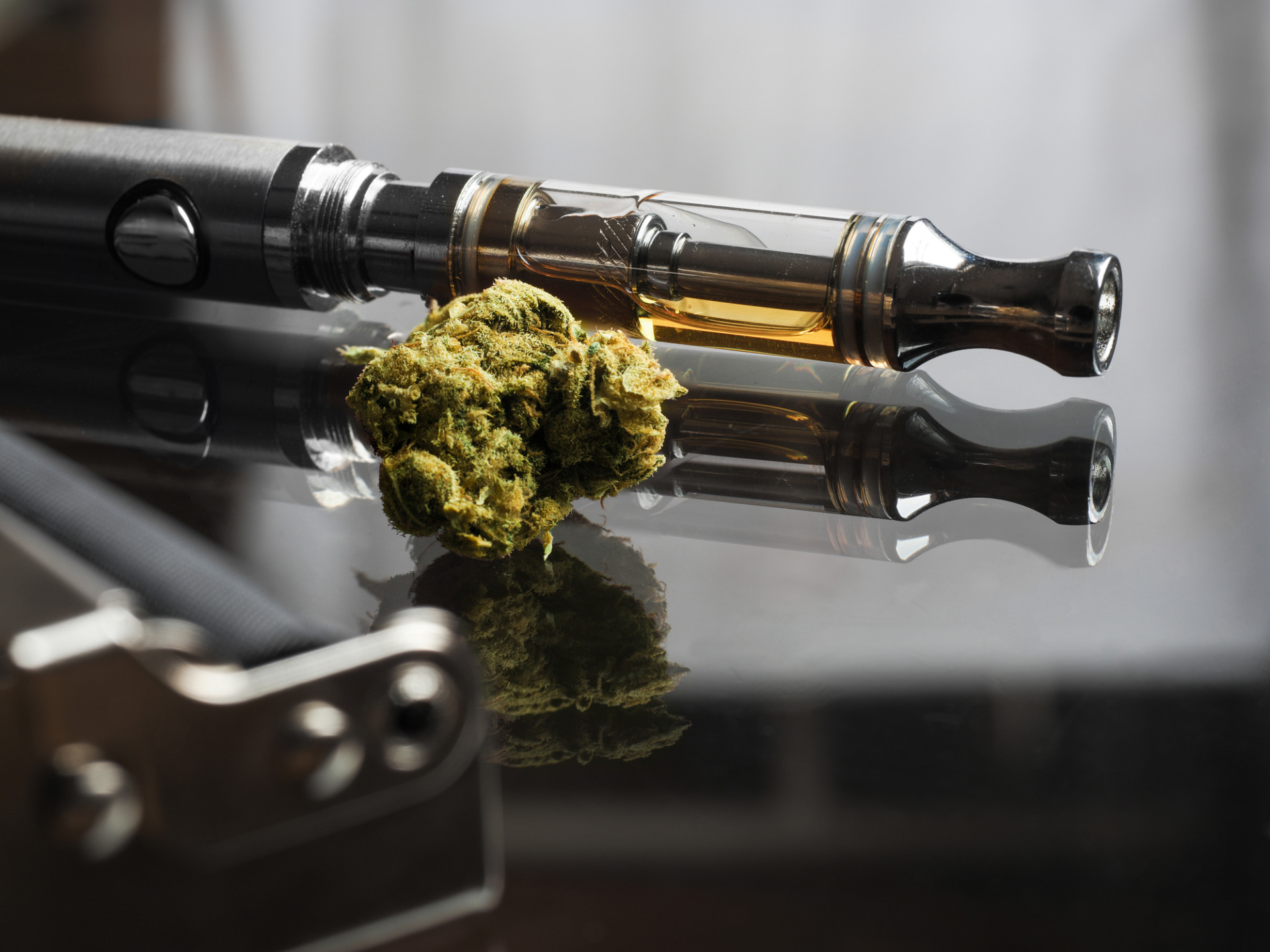 Learn 14 Close up shot of of a THCA marijuana bud with cannabis oil in cartridge of vape pen in the background.